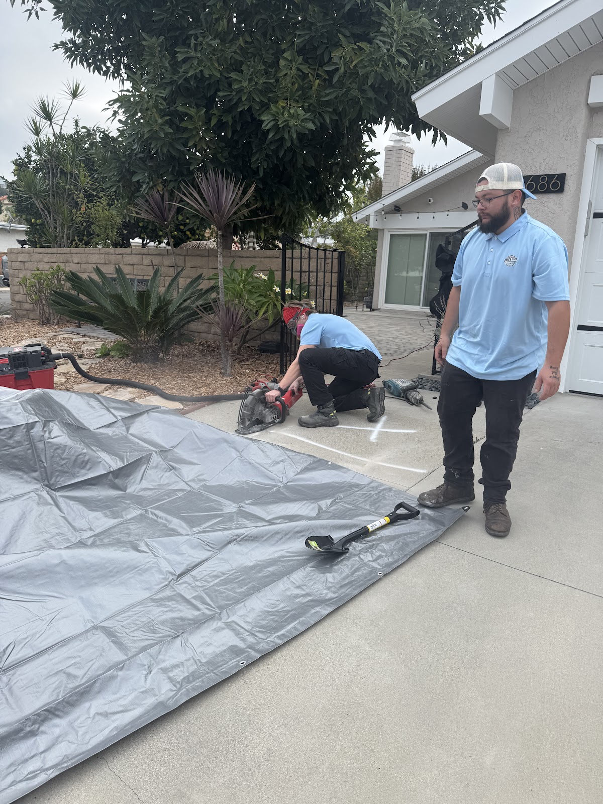 Two techs cutting a slab on a driveway, tarp down