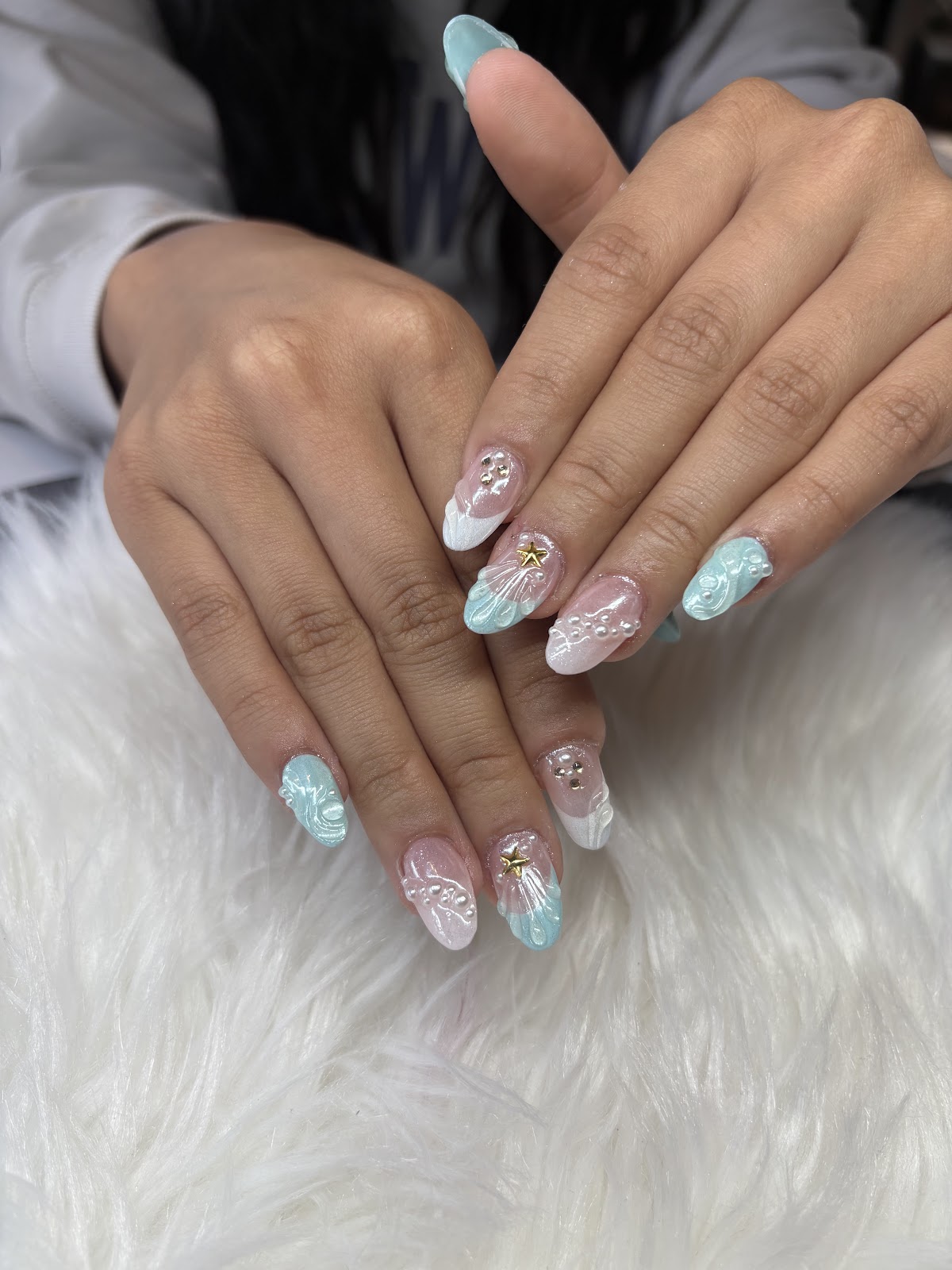 Almond nails in soft blue, pink and white with butterfly-wing detail, pearls and a gold star, by Blooming Nails