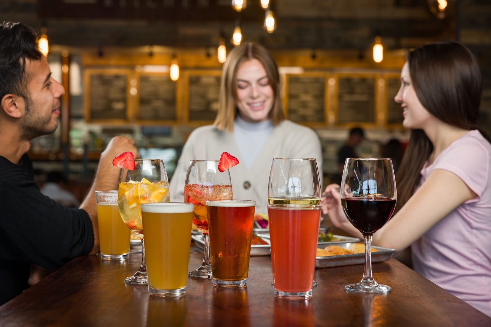 Friends at the Bushfire Kitchen counter sharing housemade lemonades, beer and wine under the warm menu-board lights