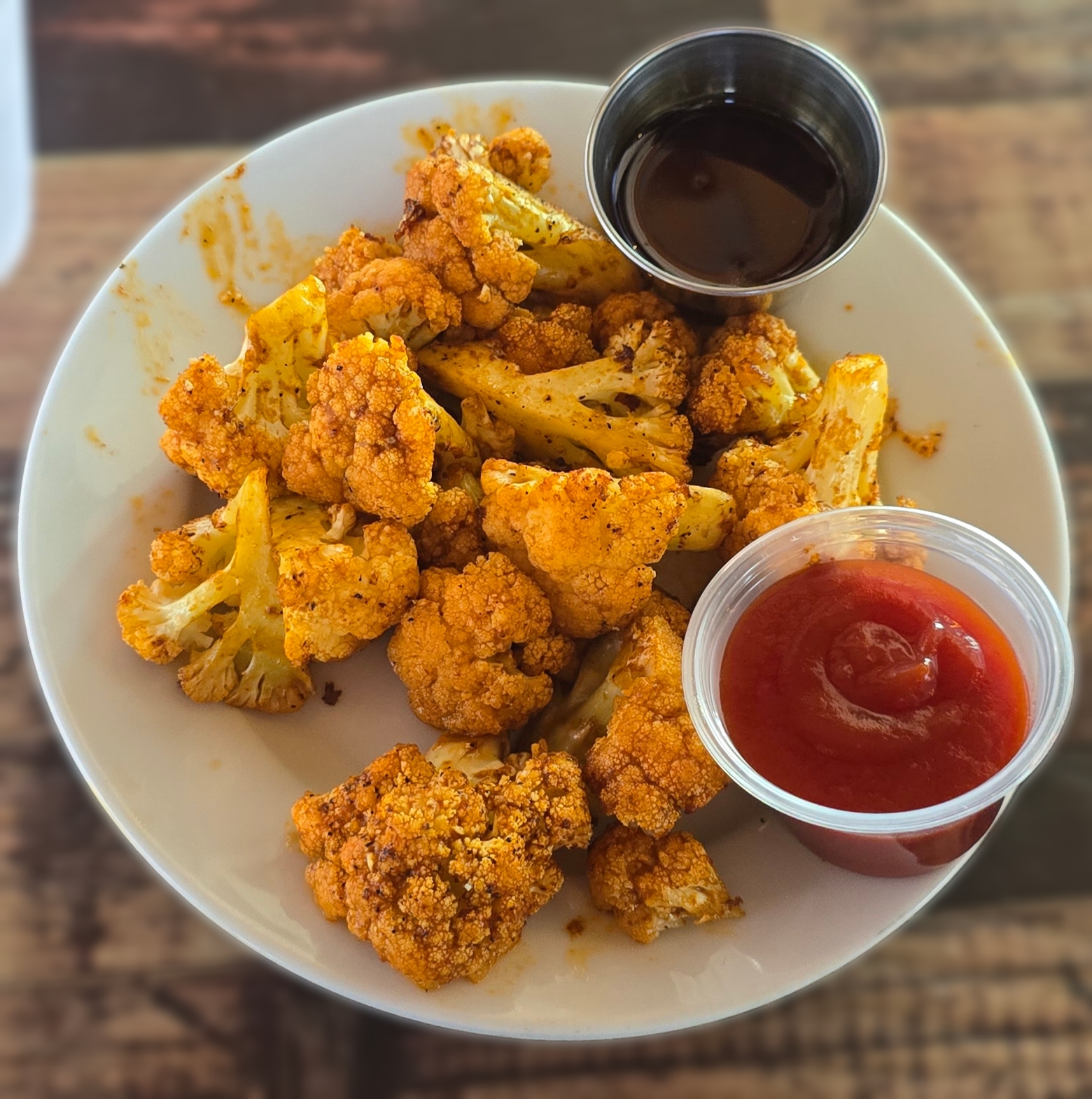 A bowl of roasted Korean cauliflower with charred edges and two dipping sauces at Bushfire Kitchen