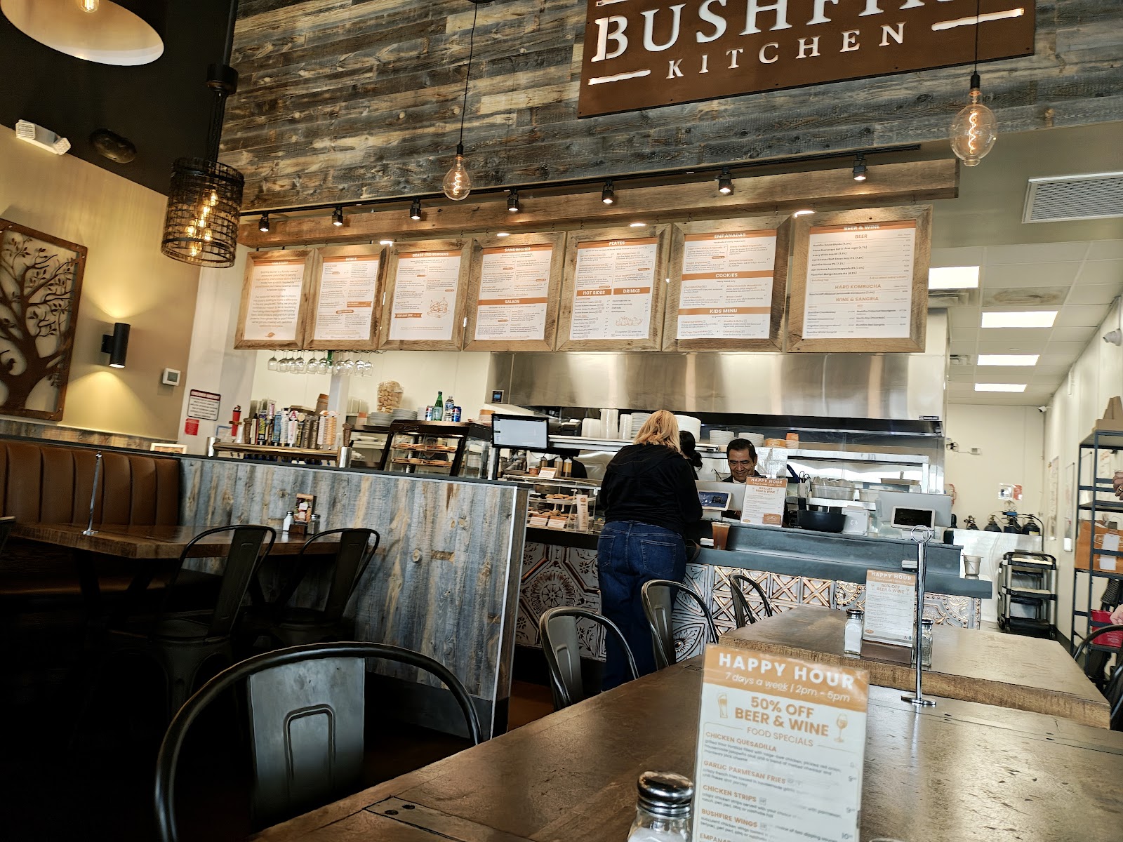 The Bushfire Kitchen Mission Viejo counter with the reclaimed-wood wall, the BUSHFIRE KITCHEN sign, and the menu boards lit by Edison bulbs