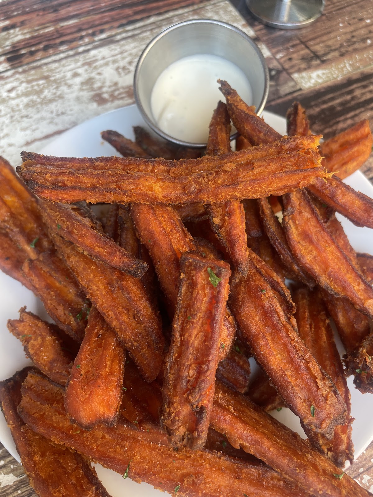A plate of golden sweet potato fries with a side of ranch on a wood table at Bushfire Kitchen