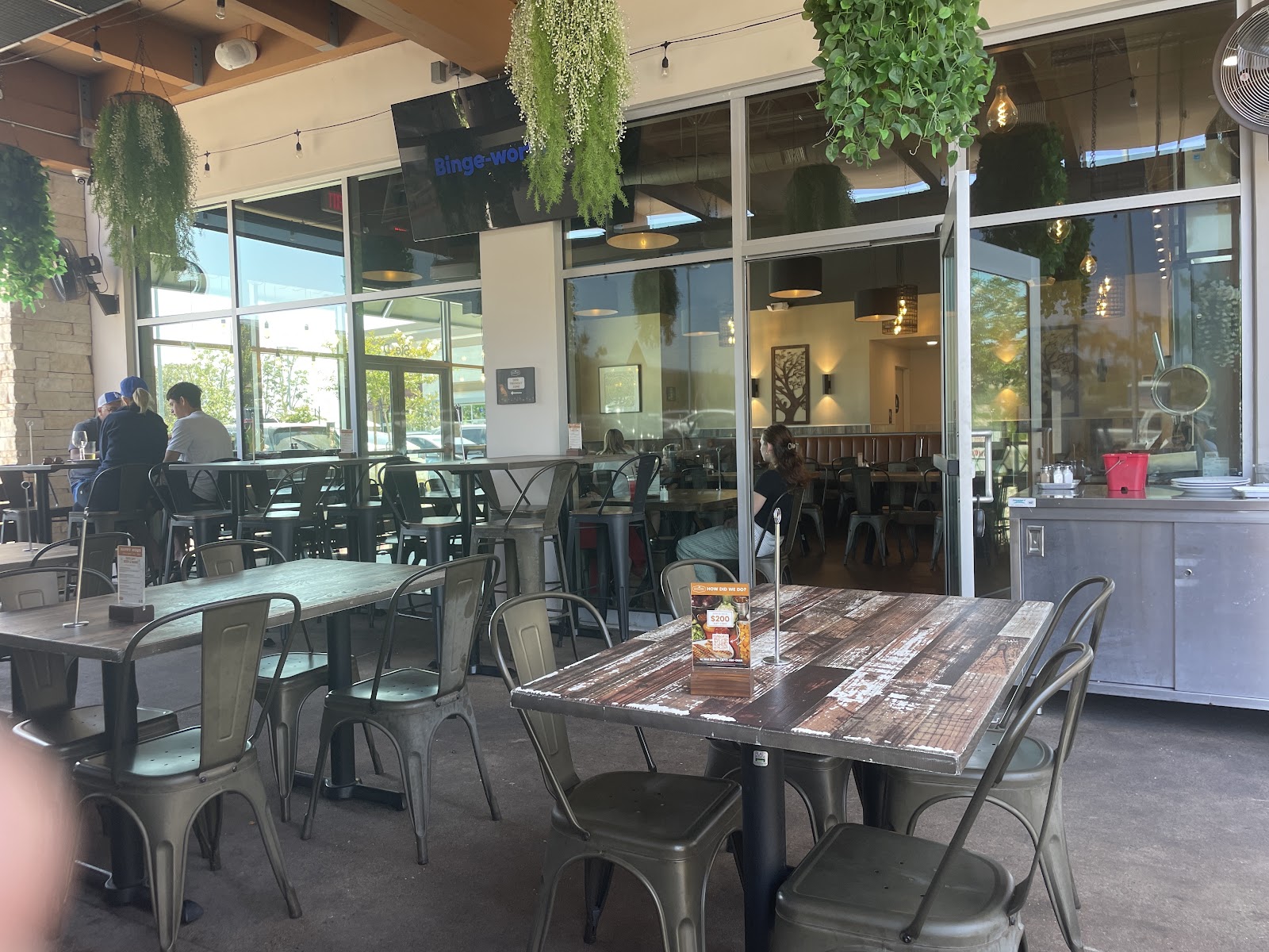 The shaded, heated patio at Bushfire Kitchen Mission Viejo with hanging greenery and metal cafe chairs