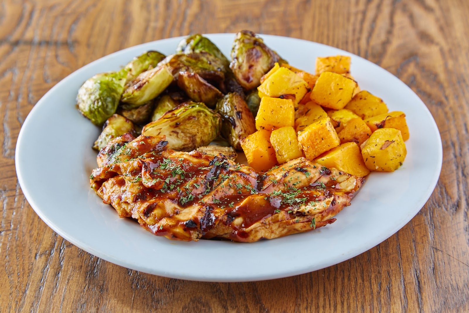 A fire-grilled BBQ chicken plate at Bushfire Kitchen with charred Brussels sprouts and roasted butternut squash on a white plate
