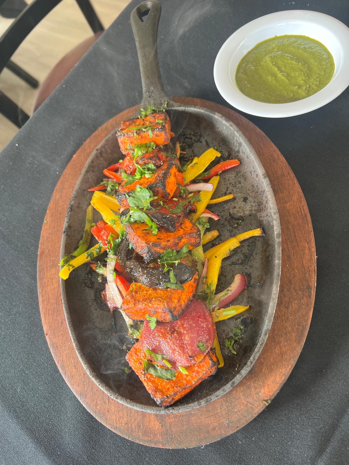 Hands lifting fresh tandoor chicken tikka above the open clay oven at Cali Curry House