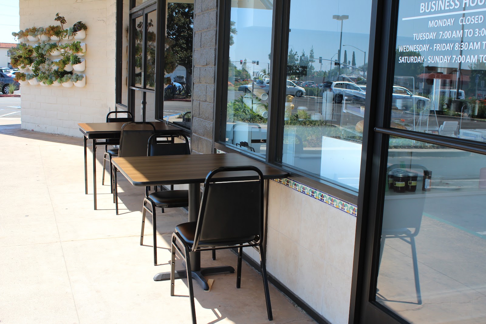 The Cloud Cafe patio with black cafe tables and chairs along the sidewalk and a green succulent wall planter beside the door