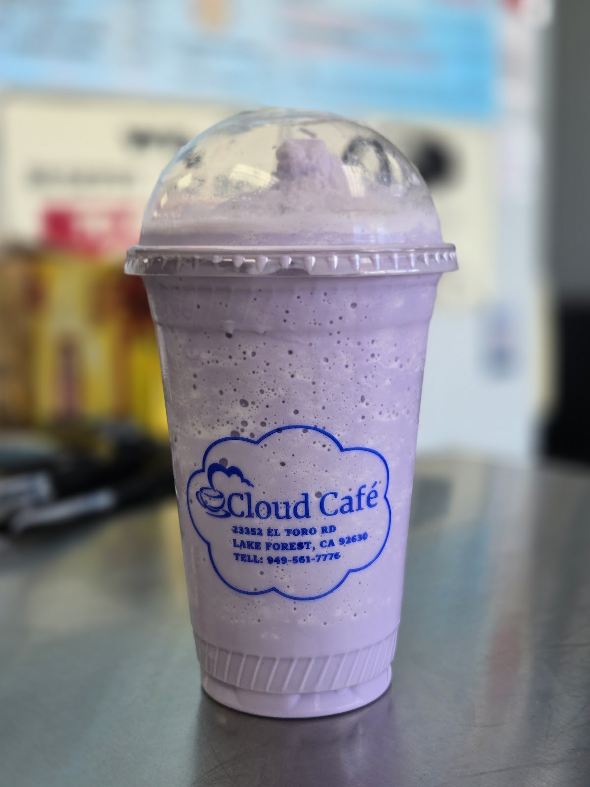 A pale lavender blended drink under a clear dome lid in a cup printed with the blue Cloud Cafe cloud-and-cup logo