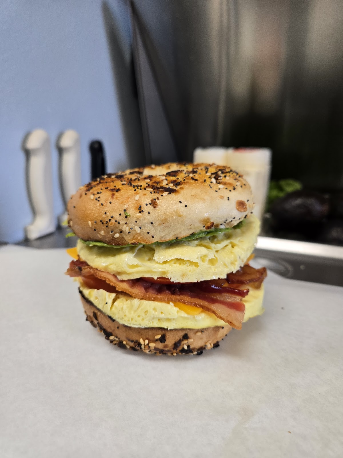 A tall breakfast sandwich on a toasted everything bagel with folded egg, bacon, cheese and greens
