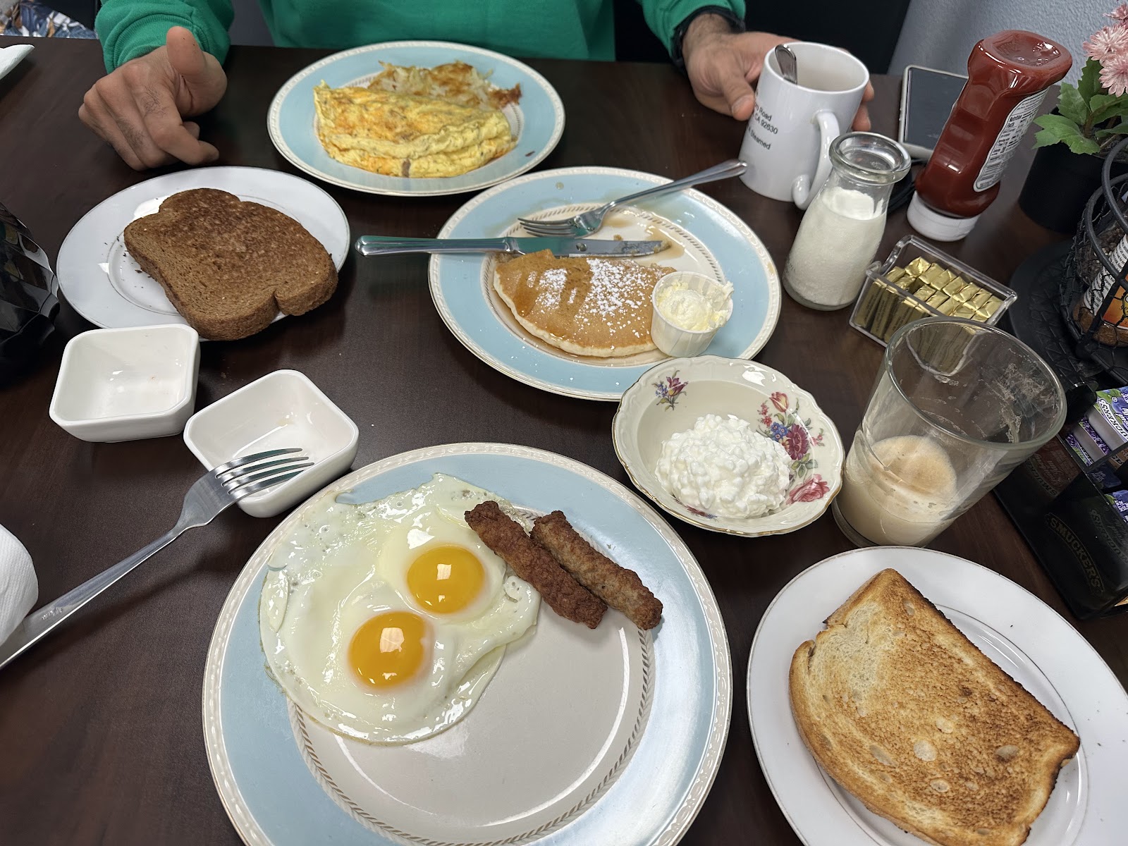 A full breakfast spread with sunny-side eggs and sausage, an omelette, pancakes with powdered sugar, toast, and the Cloud Cafe cloud mug