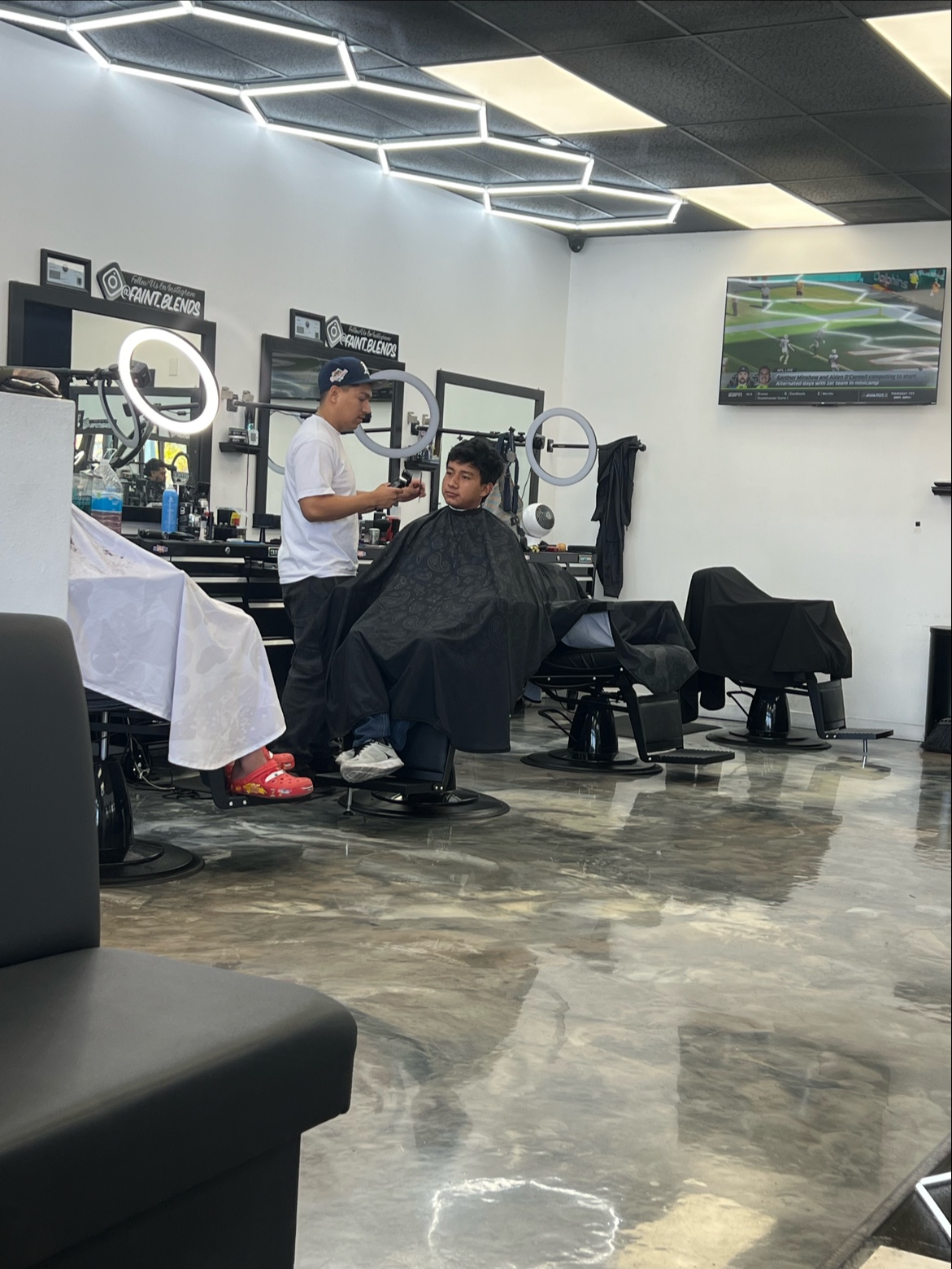 Barber mid-cut under the honeycomb LED ceiling at Faint Blends Barbershop