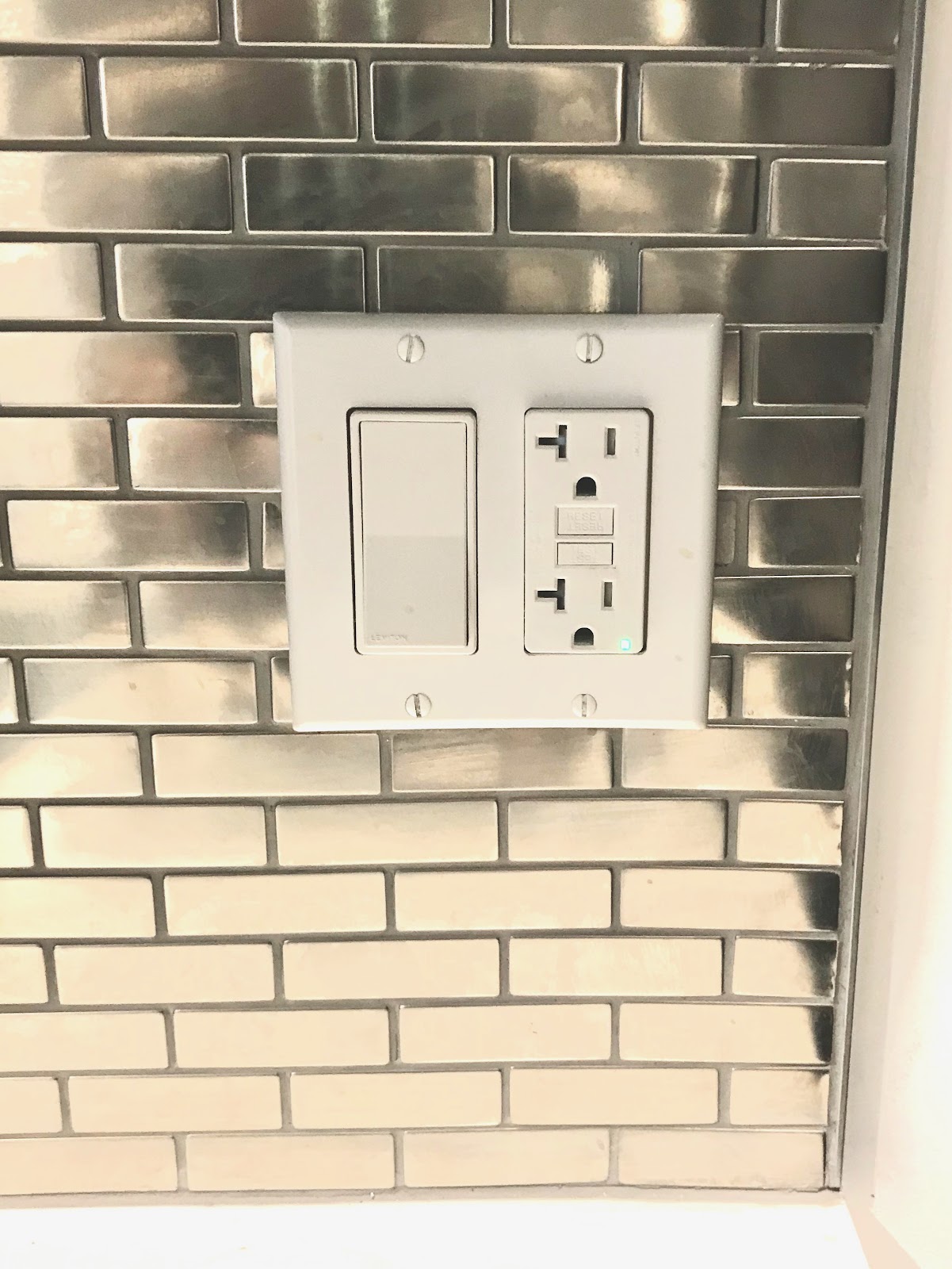 GFCI outlet and dimmer switch installed by Gerhard Electric on a stainless tile backsplash