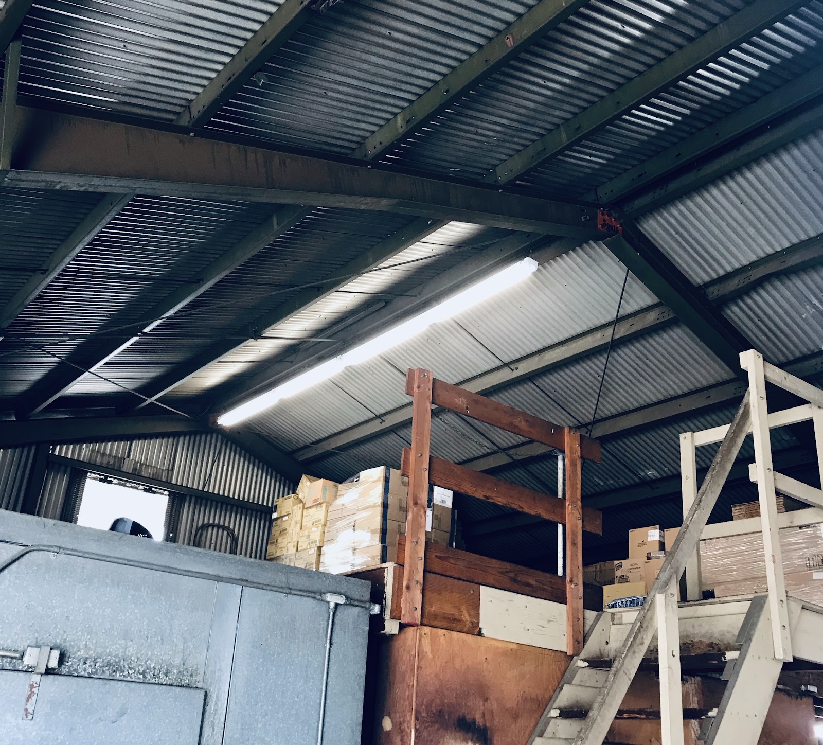 Linear high-bay fixture under a corrugated-steel warehouse roof, installed by Gerhard Electric