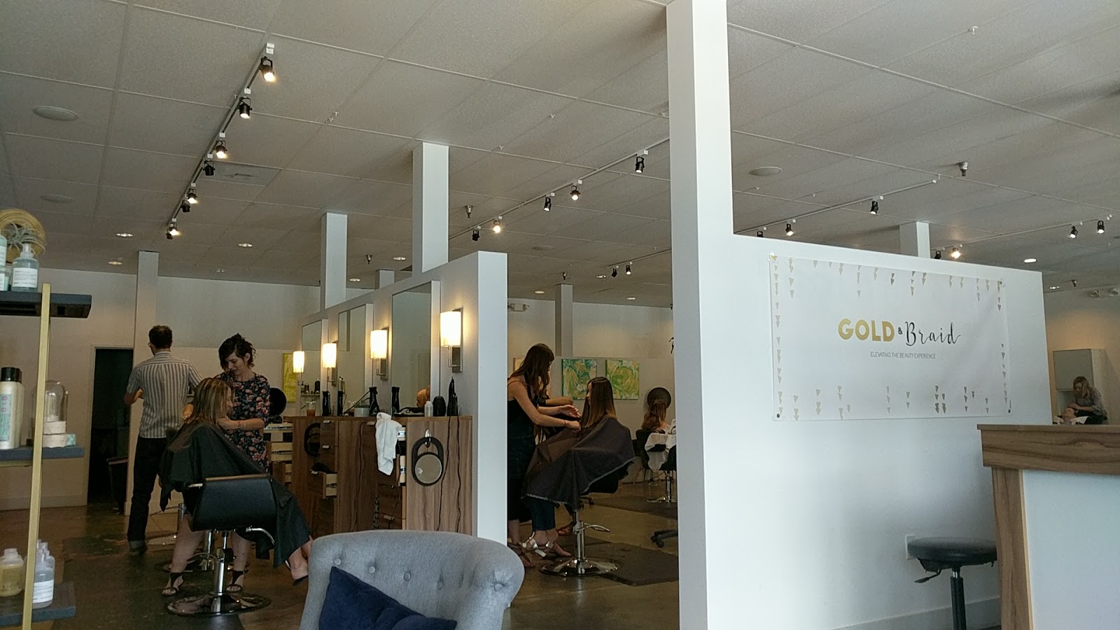 The Gold & Braid floor mid-appointment, stylists with clients beneath the gold wall banner