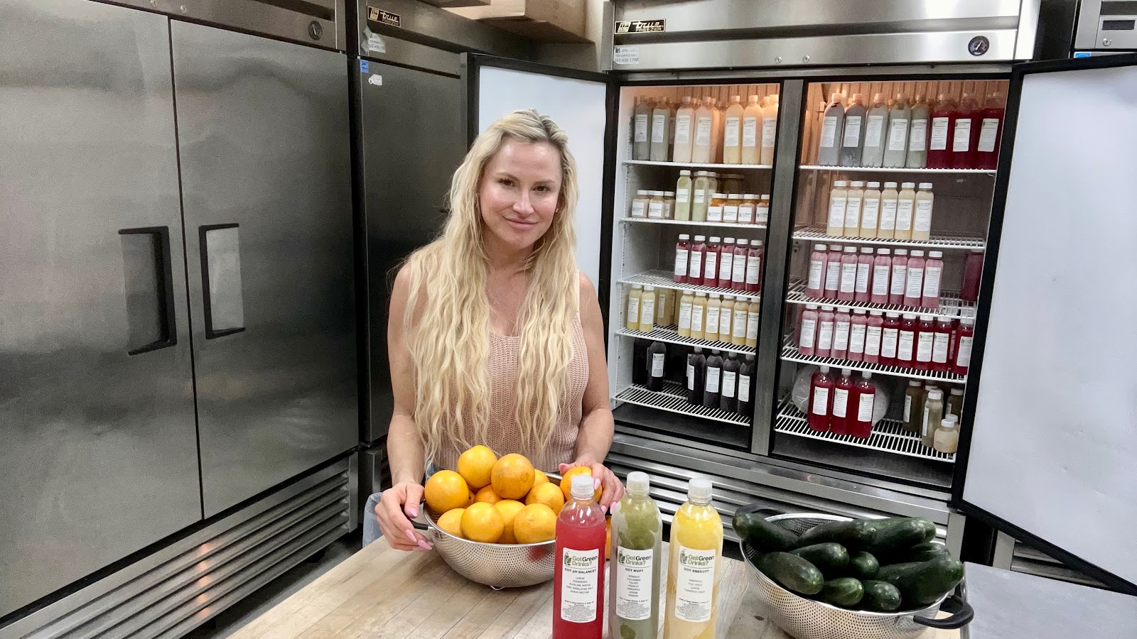 Catherine, the founder of Got Green Drinks, in the Laguna Niguel kitchen with a bowl of oranges and a fridge of fresh-pressed juice behind her
