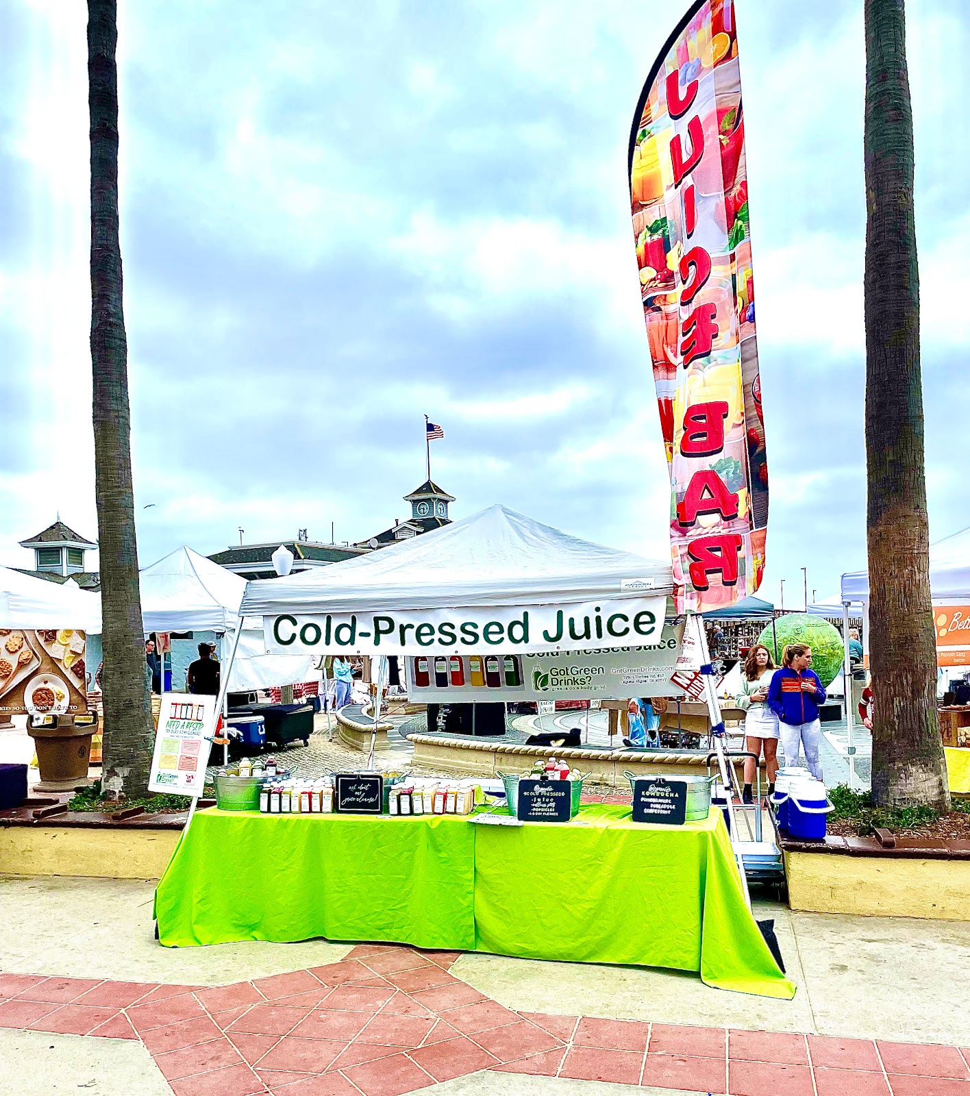 The Got Green Drinks farmers market tent with a Cold-Pressed Juice banner and a Juice Bar feather flag, the table draped in bright green