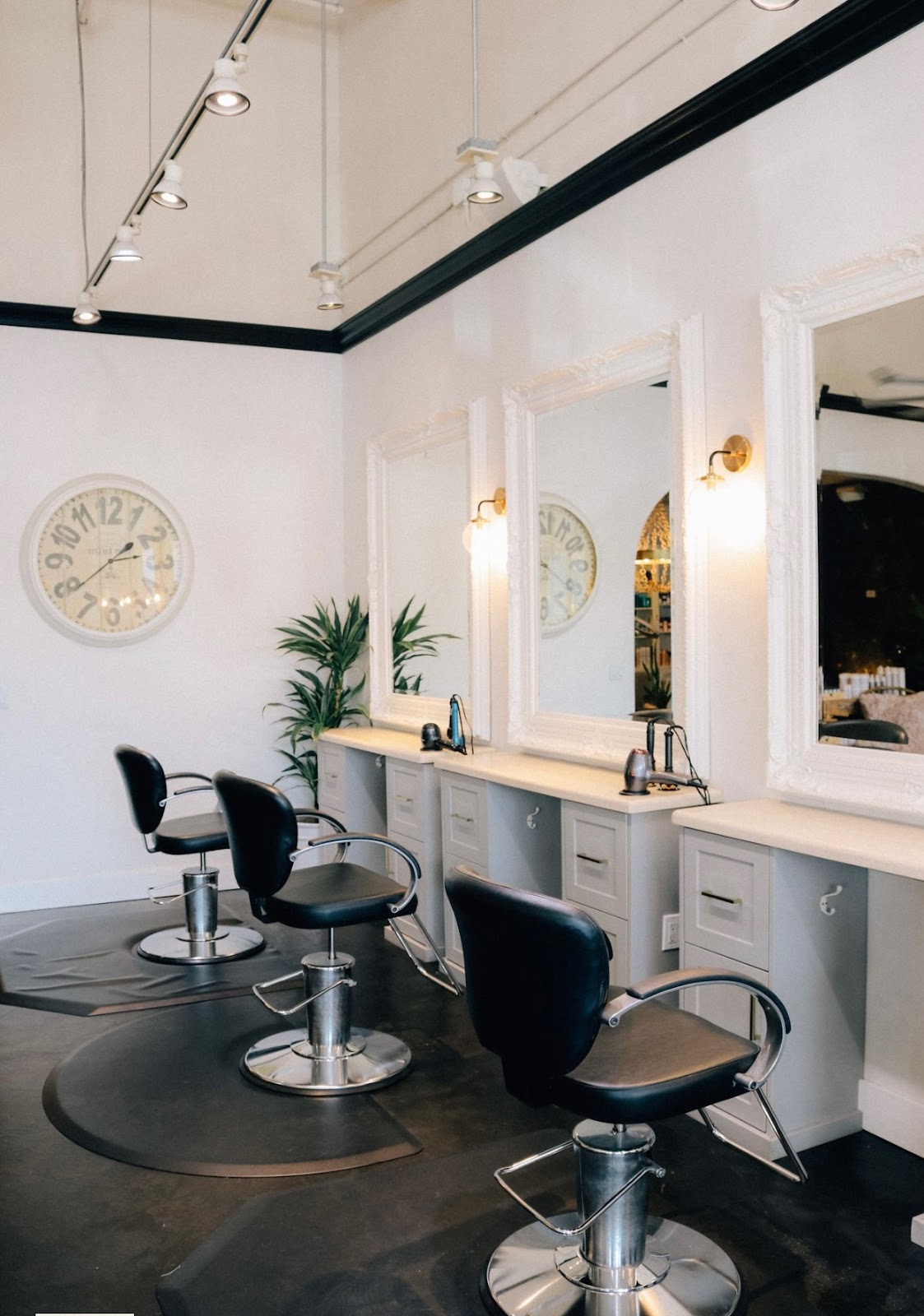 Styling stations at H Studio with ornate white-framed mirrors, black salon chairs, polished concrete floor and a large wall clock