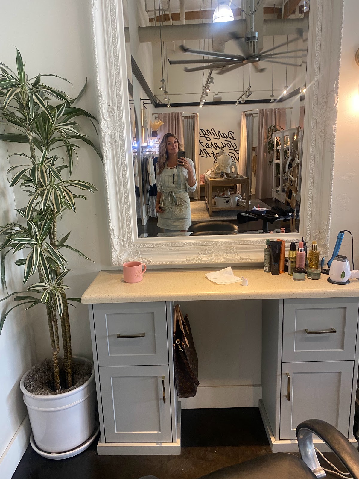 A styling station at H Studio reflected in an ornate white-framed mirror, with the 'darling you are loved' wall script visible behind