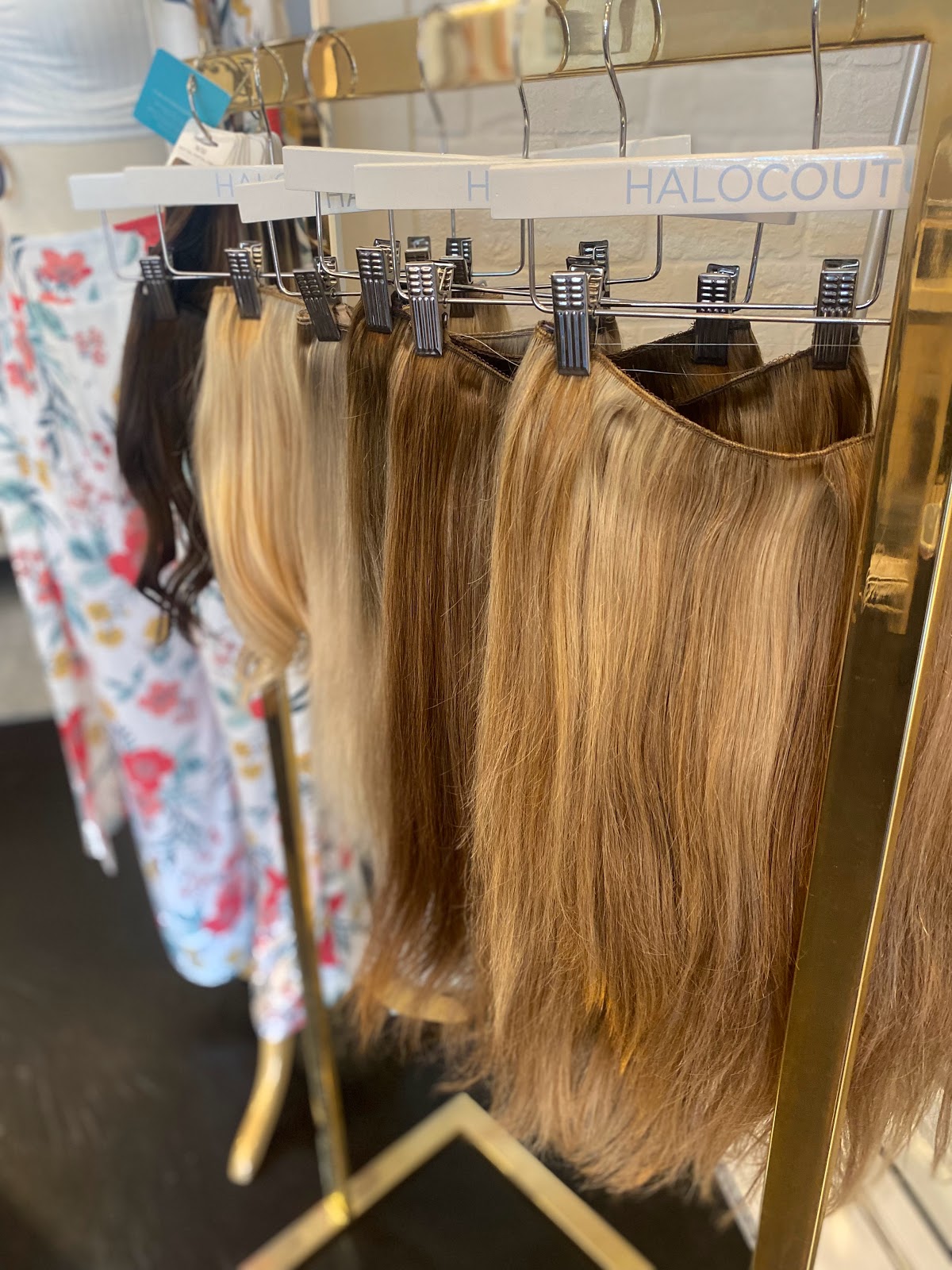 Halo Couture hair extensions in several blonde and brown shades hanging on a gold display rack at H Studio