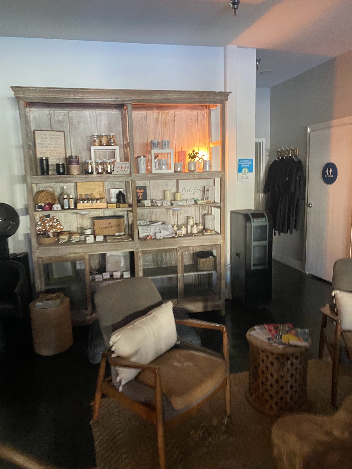 A reclaimed-wood retail hutch in the H Studio boutique stocked with candles, mugs and gifts, beside mid-century lounge seating