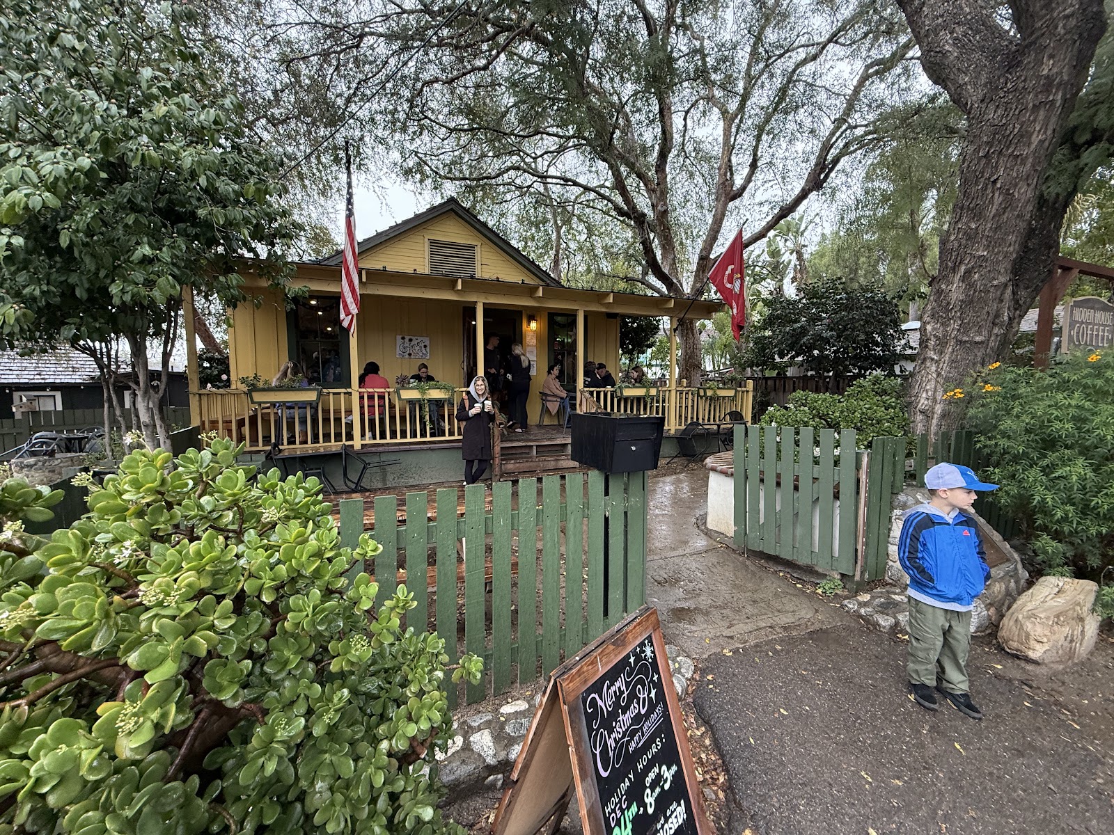 The wooden cottage of Hidden House Coffee on Los Rios Street, with the sandwich board out front and customers on the porch