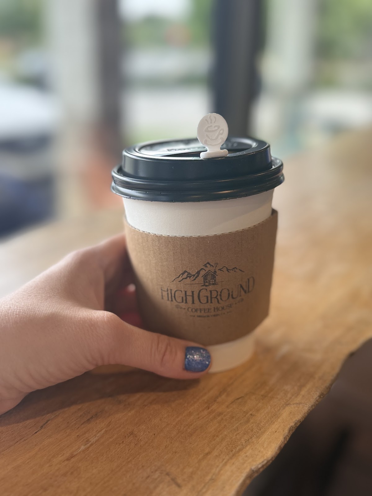 A High Ground cup in hand, kraft sleeve, navy cabin logo