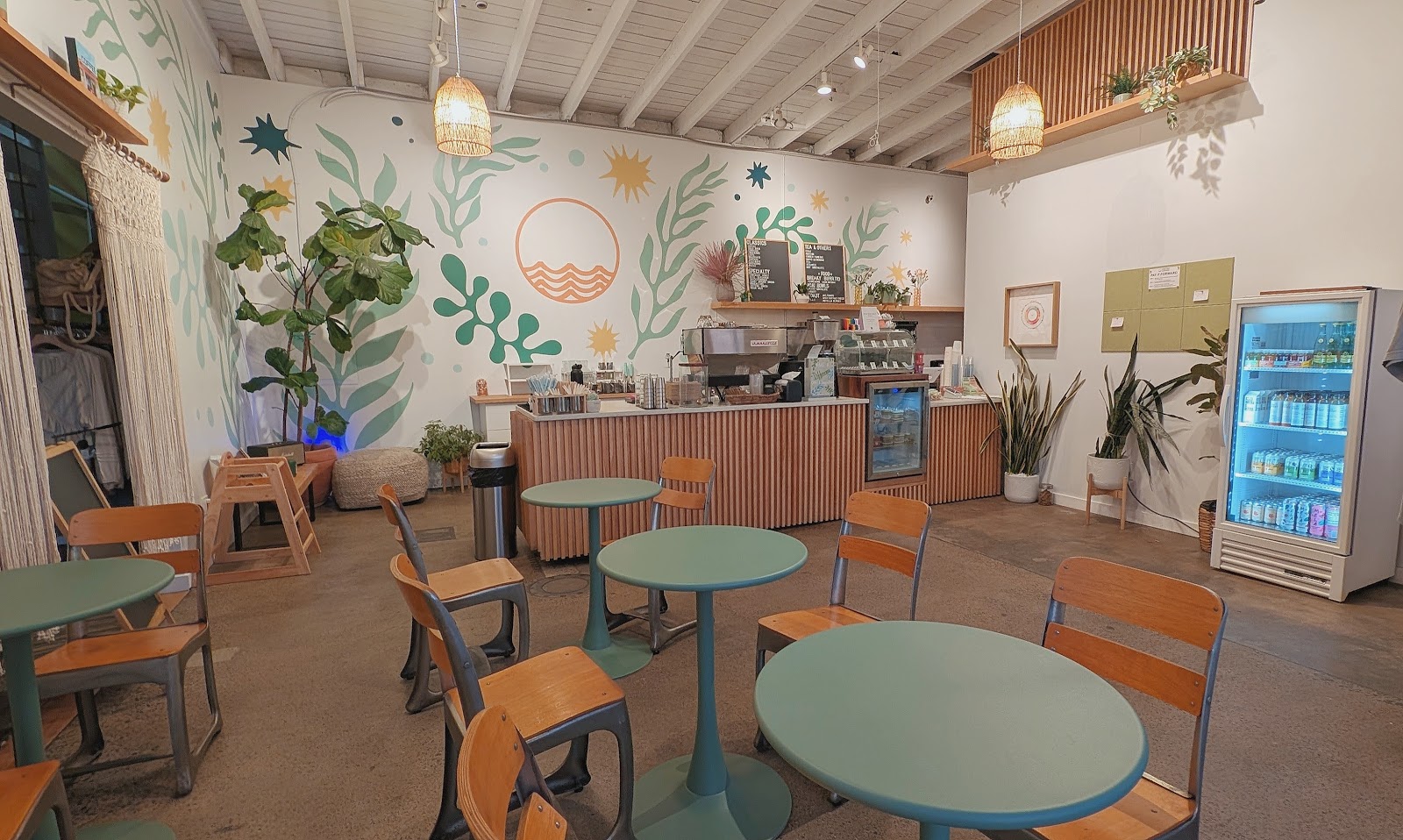 The sunny mural-painted interior of High Tide Coffee in Laguna Niguel, with sage tables and ocean-wave wall art
