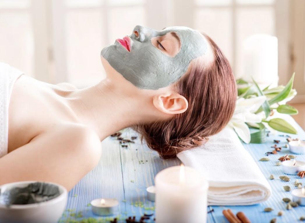 A guest relaxing during a clay mask facial surrounded by lilies and candles