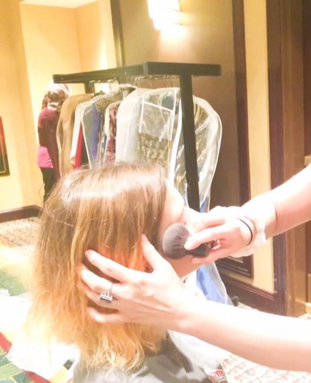 Bridal makeup being applied at Honey + Cream Spa, with a rack of gowns behind
