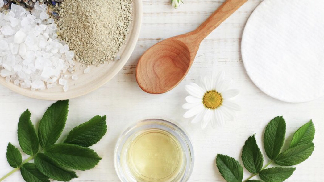 Clay, sea salt, facial oil and chamomile laid out on a light table at Honey + Cream Spa