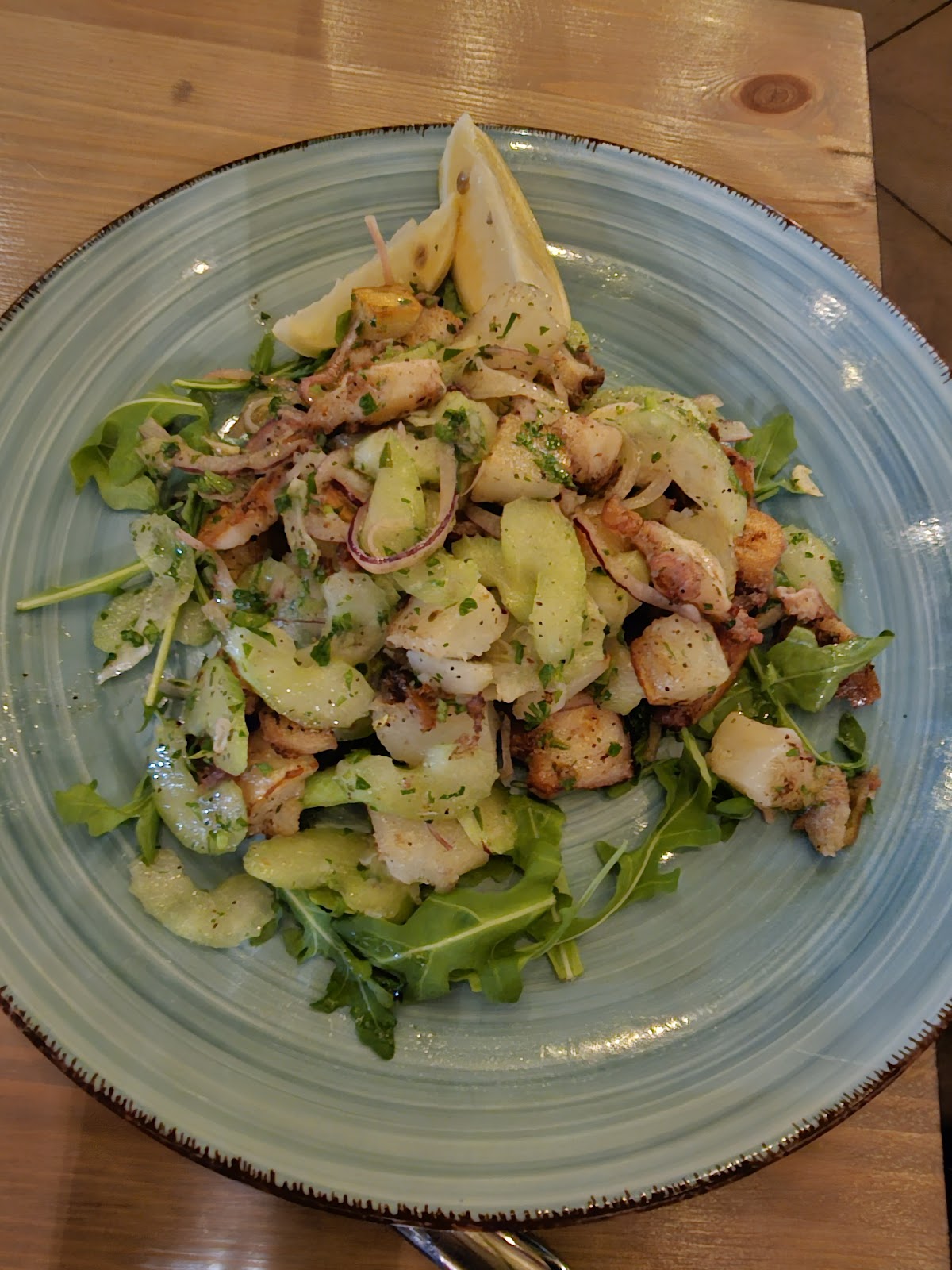 Grilled octopus salad with arugula, potato, shaved fennel and lemon on a blue ceramic plate over a wood board