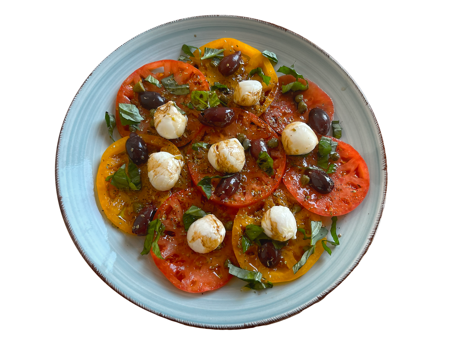 Heirloom caprese with red and yellow tomato slices, mozzarella pearls, Kalamata olives and basil on a pale blue plate