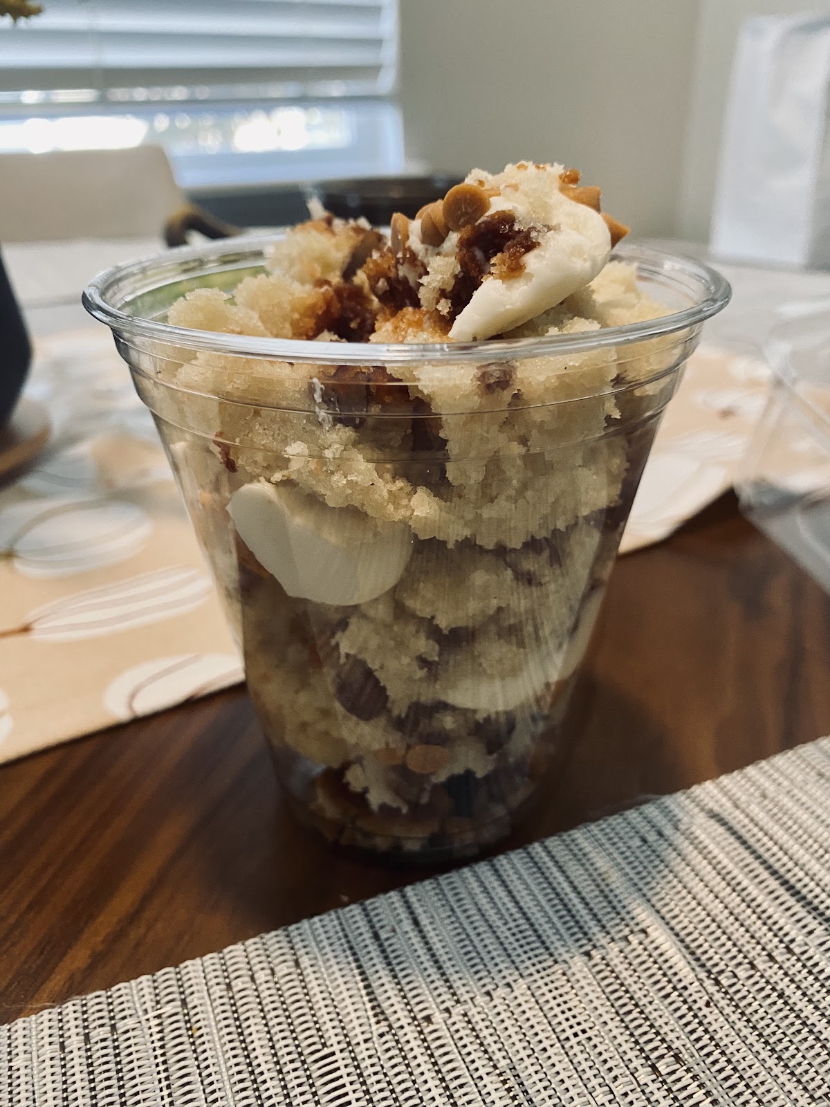 A cake in a cup from A Little Something Sweet, layered cake and cream topped with toasted almonds and caramel in a clear cup