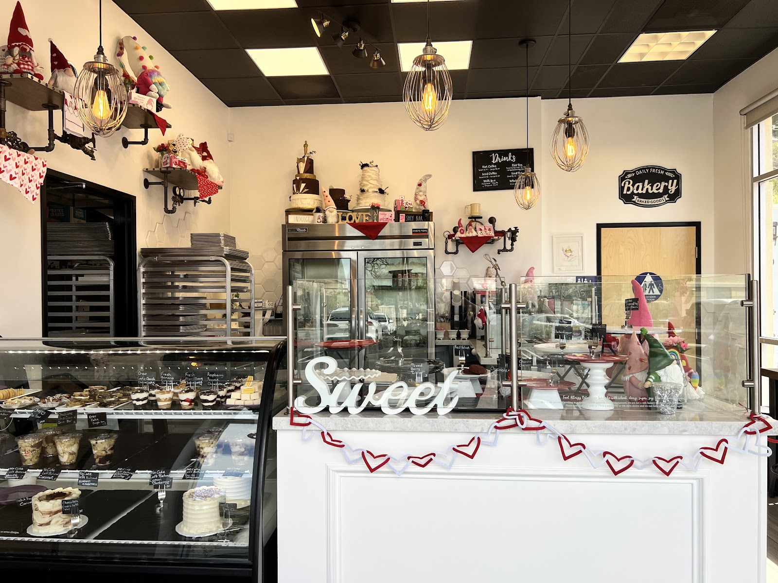 The interior counter of A Little Something Sweet with a white pastry case, a Sweet sign, hanging bulb lights and cheerful decor