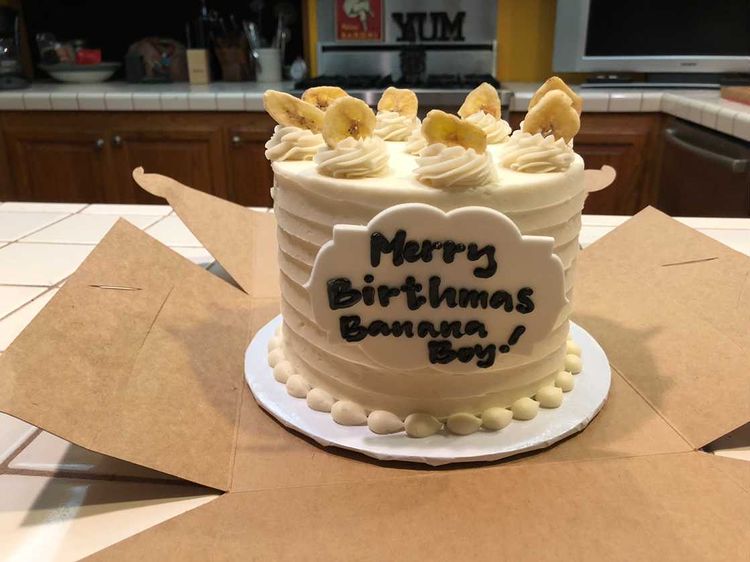 A custom banana cream celebration cake with cream rosettes and banana chips, hand-lettered with a personal message
