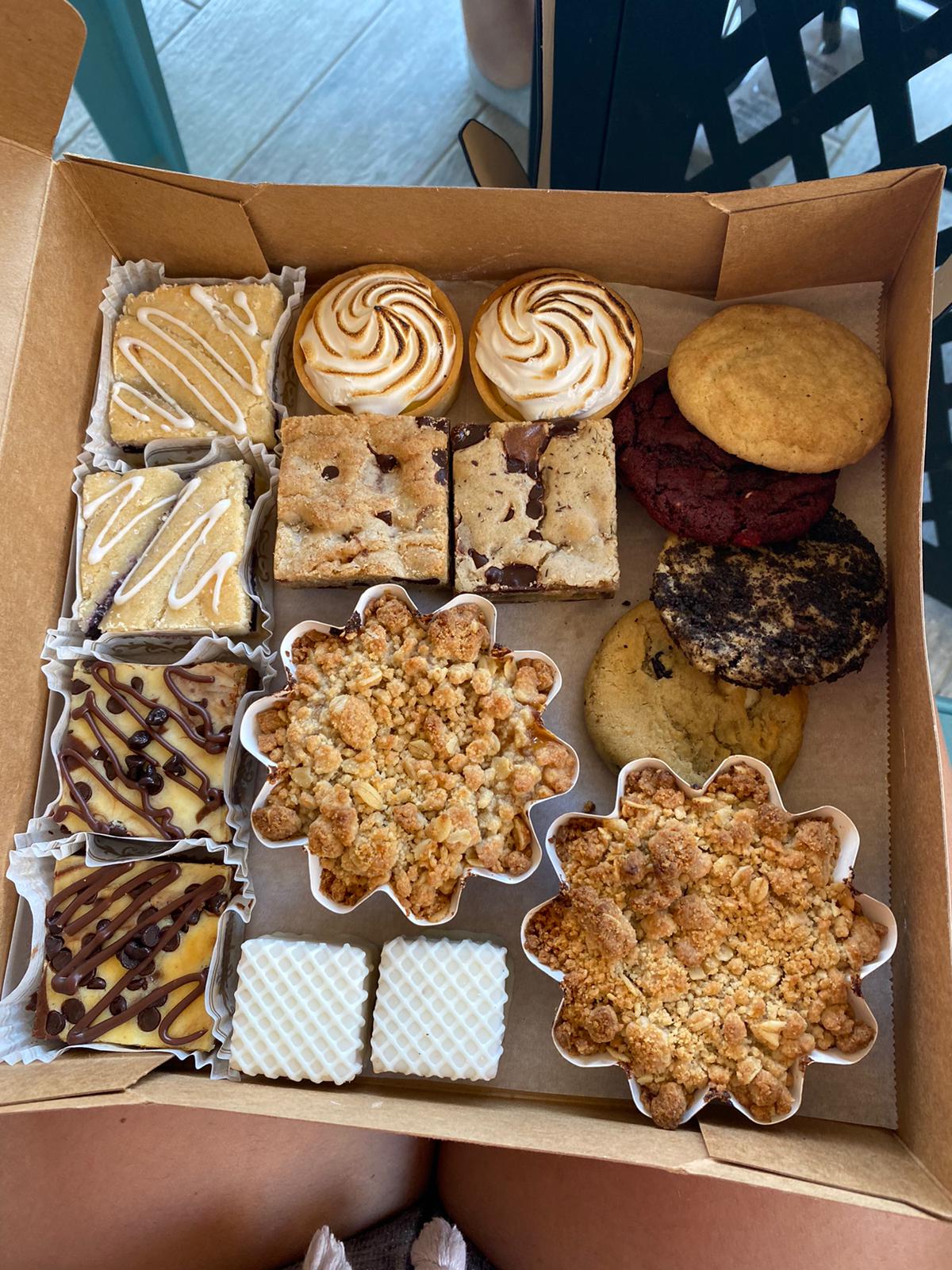 A bakery box filled with cheesecake bars, lemon meringue tarts, blondies, fruit crumb tarts and cookies from A Little Something Sweet
