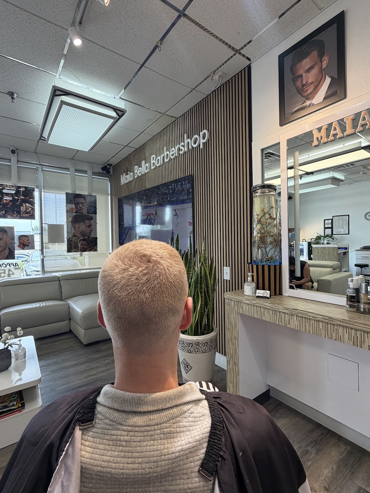 A clean blonde buzz from behind at Maia Bella, the slatted-wood feature wall and Maia Bella Barbershop sign behind