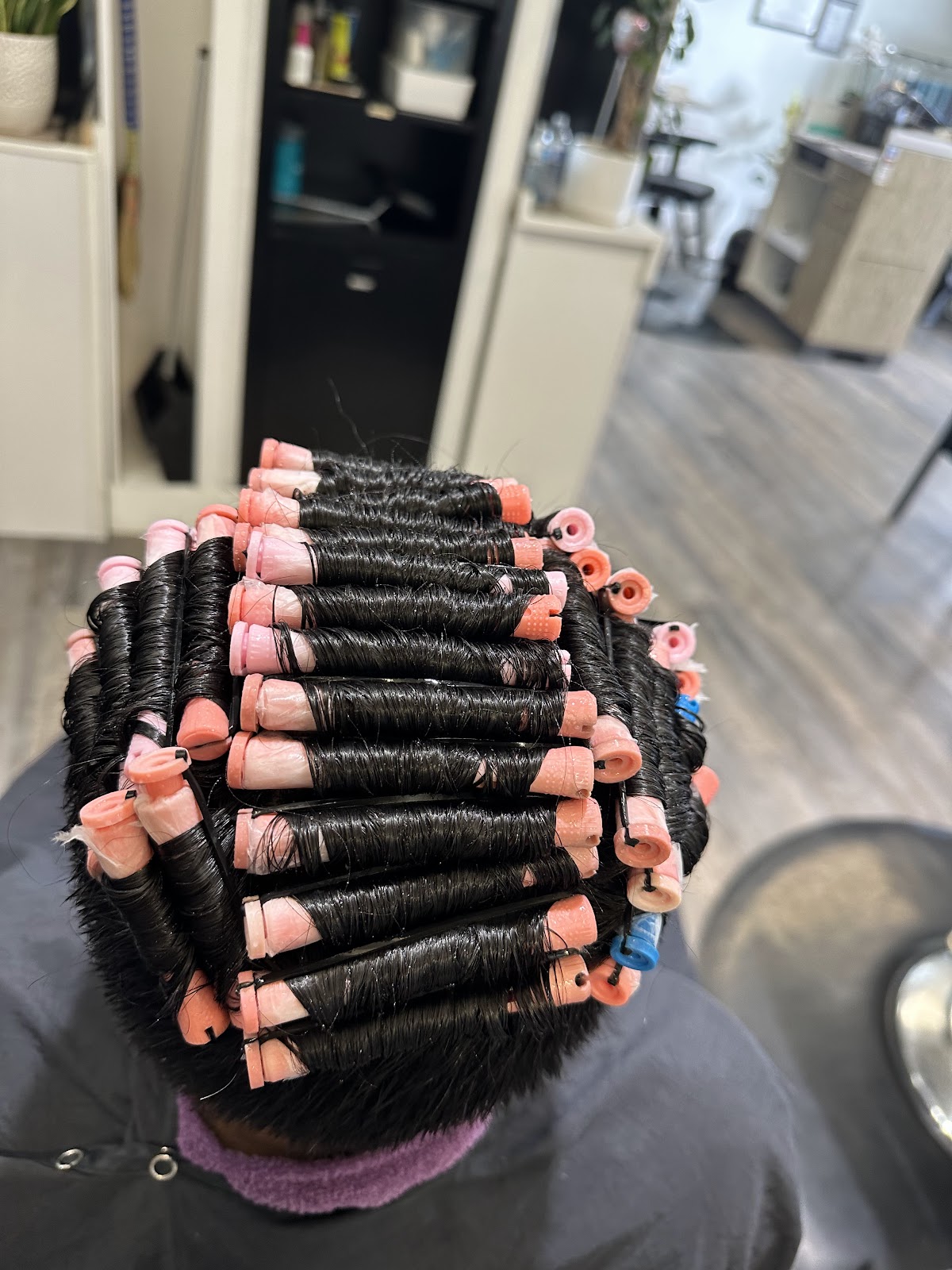 Pink perm rollers set on dark hair at Maia Bella, a perm in progress