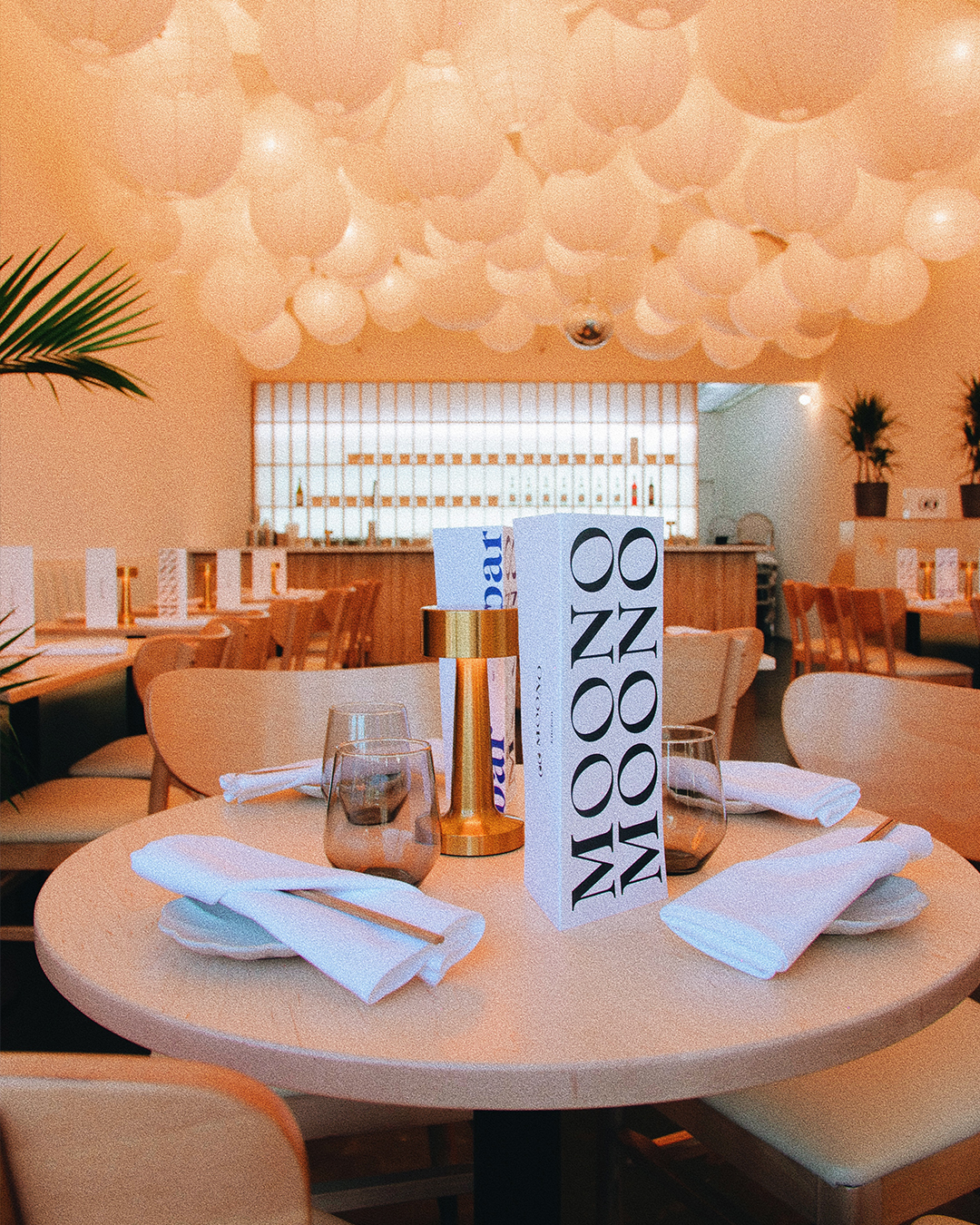 A close-up of a dining table at MOONO with the tall MOONO MOONO menu card standing upright in black sans on cream paper