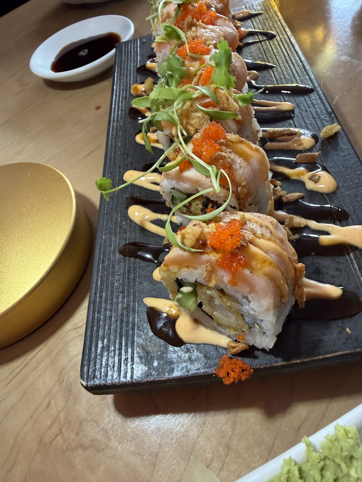 Salmon Volcano Roll at MOONO. Tempura shrimp, cucumber, crispy onion inside; seared salmon, spicy mayo, eel sauce, masago, microgreens on top. Plated on slate.