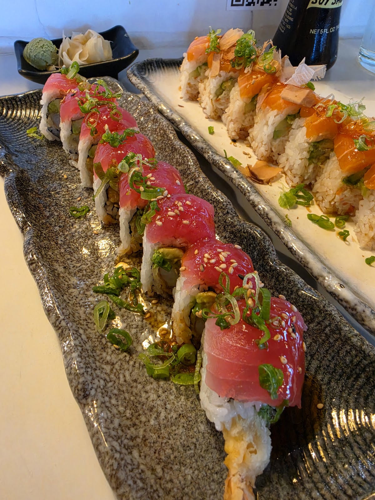Two long slate plates of Muse Sushi House specialty rolls topped with sliced tuna and salmon