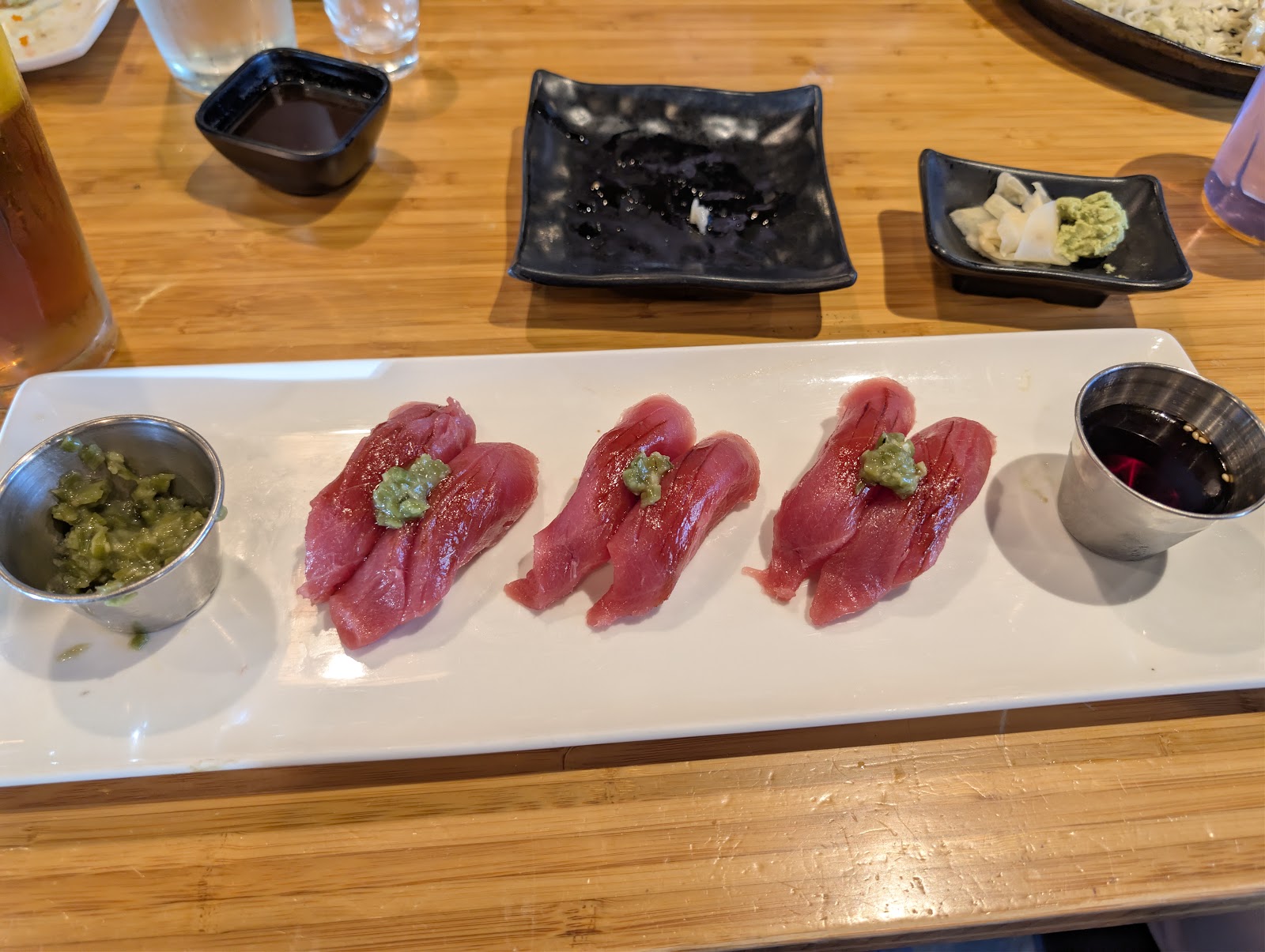 Three pieces of fresh tuna nigiri topped with wasabi on a white plate at Muse Sushi House