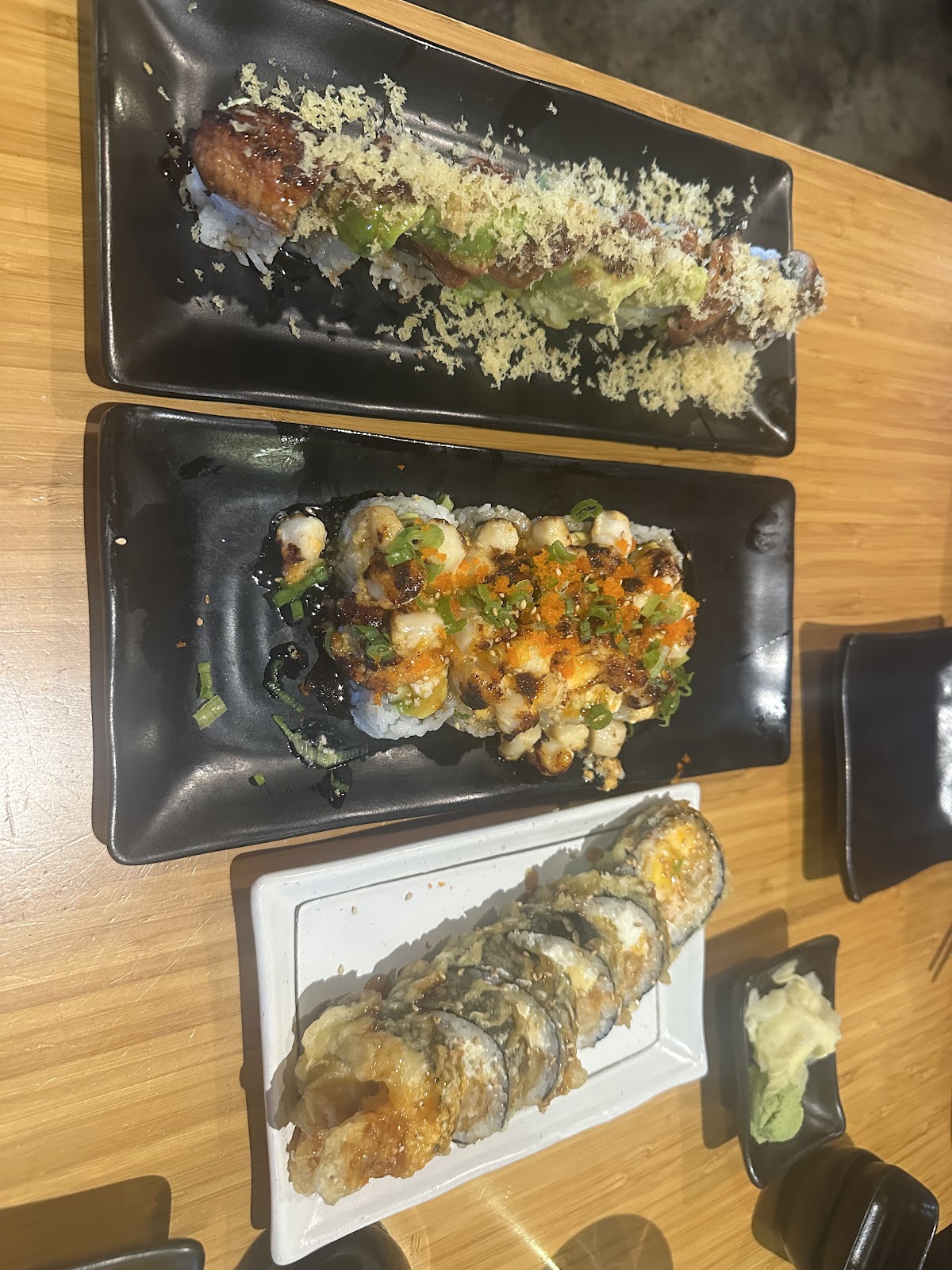 An overhead view of three Muse Sushi House specialty rolls plated on black and white rectangular dishes