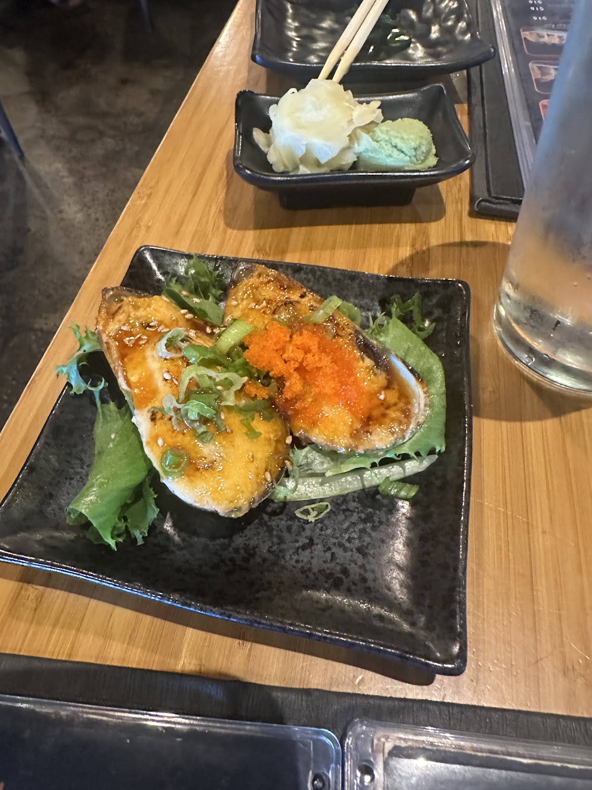 Two baked mussels topped with masago and scallion on a black plate at Muse Sushi House