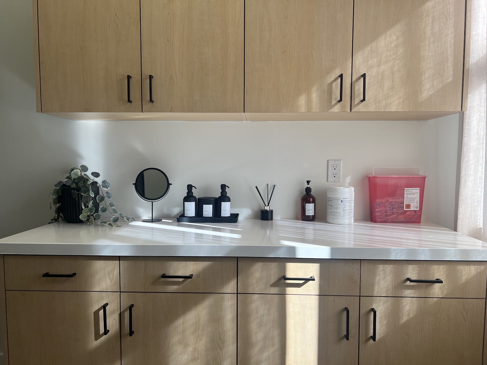 Treatment cabinetry in light oak with black hardware and amber dispensers at NakedMD