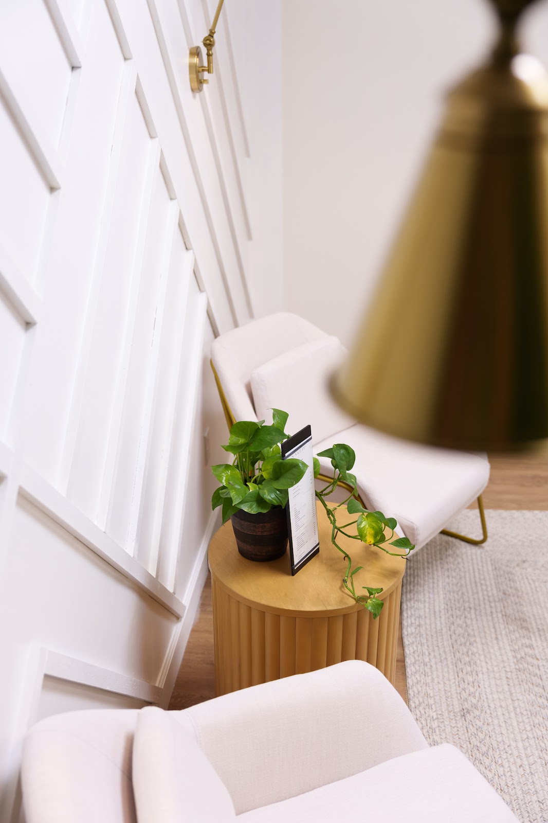 A bright corner of NakedMD with cream chairs, a brass sconce, and a fluted oak side table
