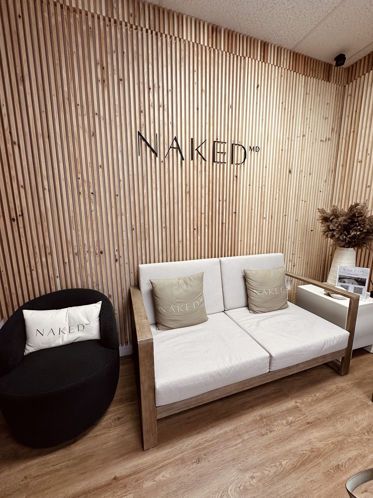 The NakedMD lobby with a light wood-slat wall, the black NAKED MD mark, a black boucle chair and a cream sofa