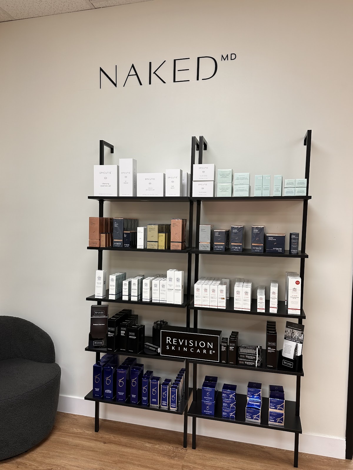 Black ladder shelving at NakedMD stocked with ZO Skin Health, Revision Skincare, and Epicutis under the NAKED MD wall mark