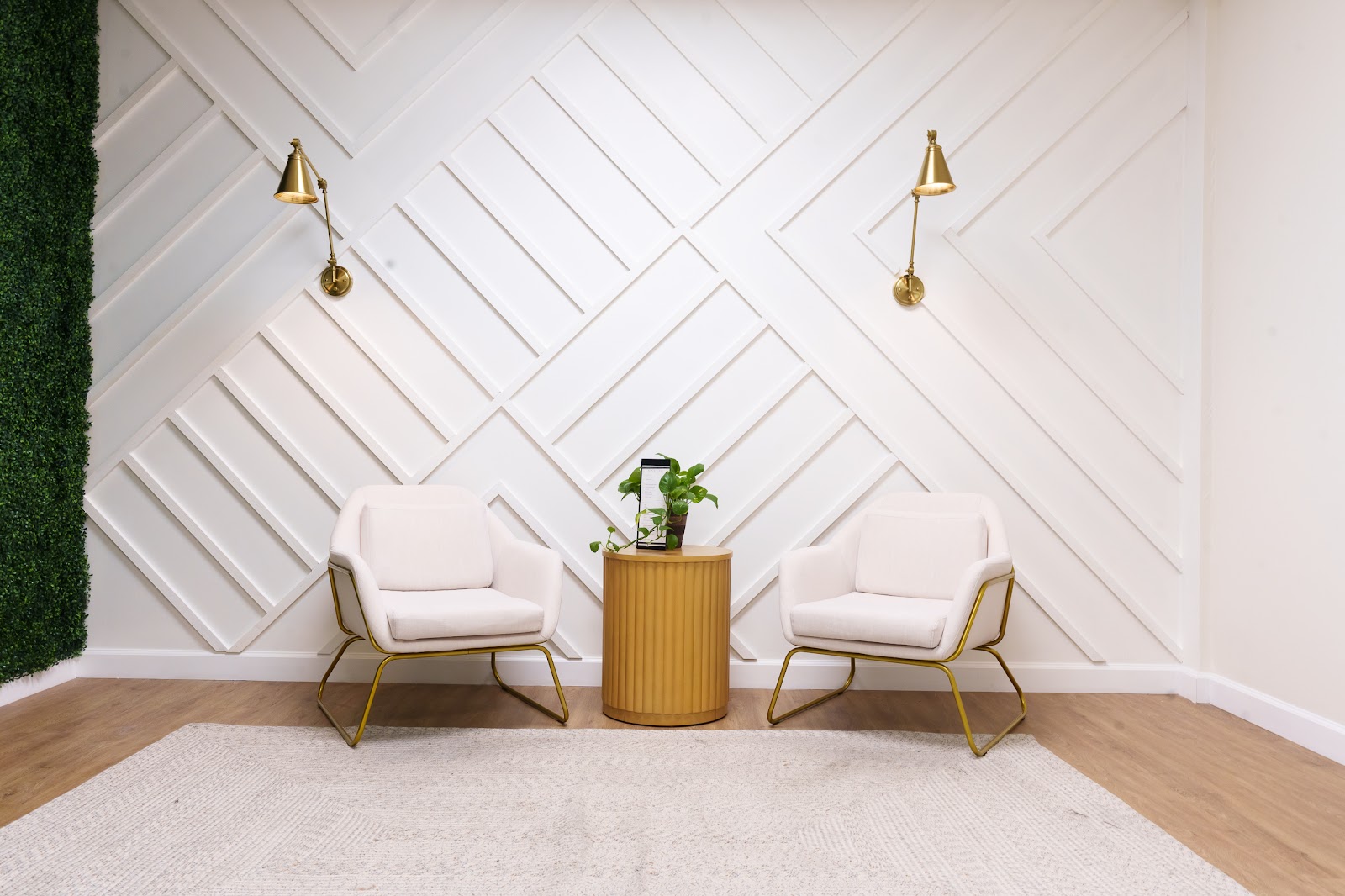 The NakedMD Mission Viejo waiting room: a white diagonal panelled accent wall with brass sconces, two cream chairs and a fluted oak side table on a soft rug