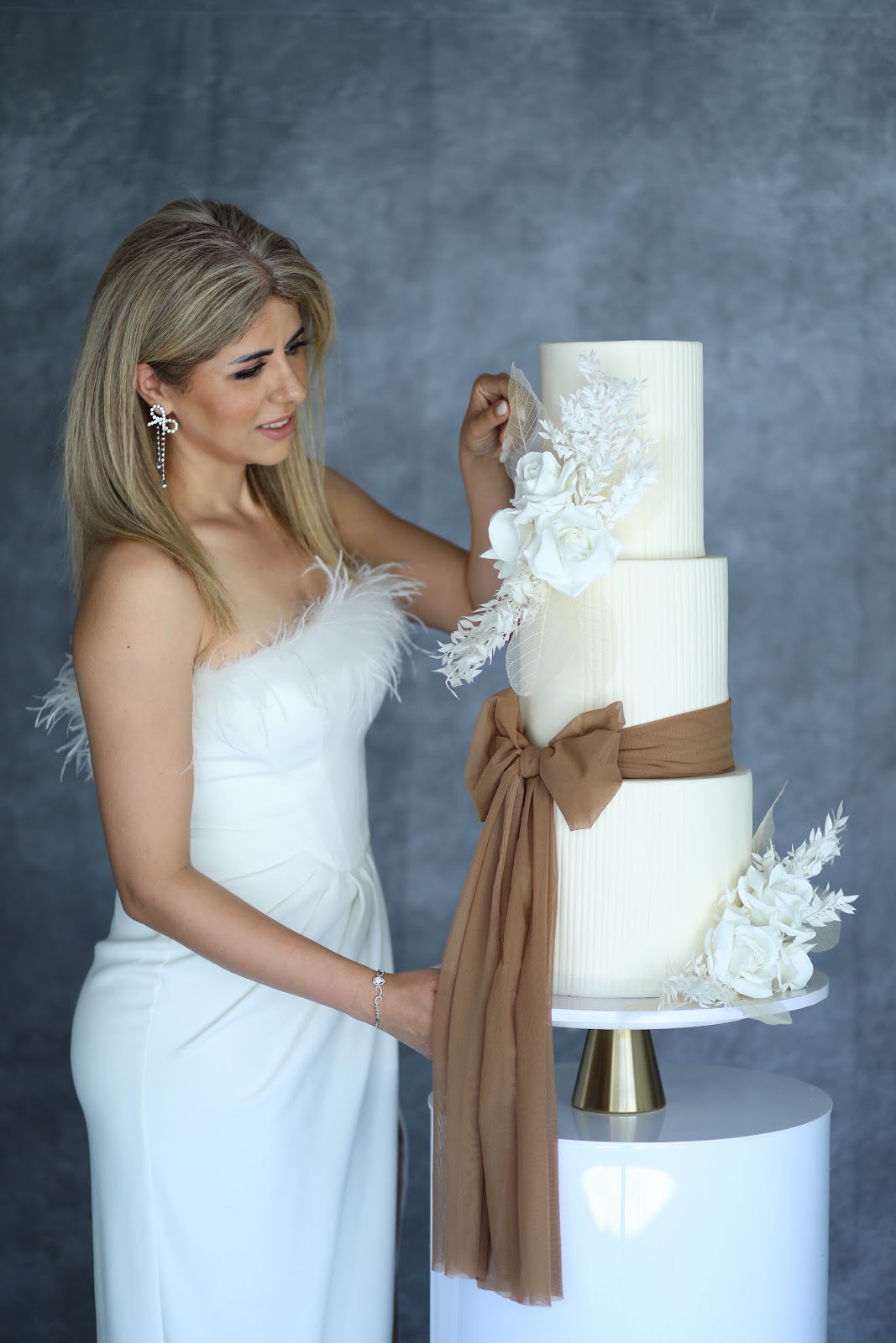 Nikoo Vahdat, founder of NikooCake, styling a three-tier ivory wedding cake with a copper sash and sugar florals