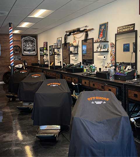 The row of barber chairs at Offshore, OFFSHORE-branded chair capes folded over each
